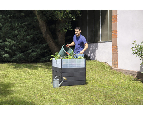 Hochbeet aus Holzimitat mit Mann, der Pflanzen einsetzt, und Giesskanne im Garten