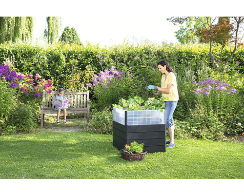 Garten mit Hochbeet, sitzendem Kind auf einer Bank und einer Frau, die im Hochbeet arbeitet