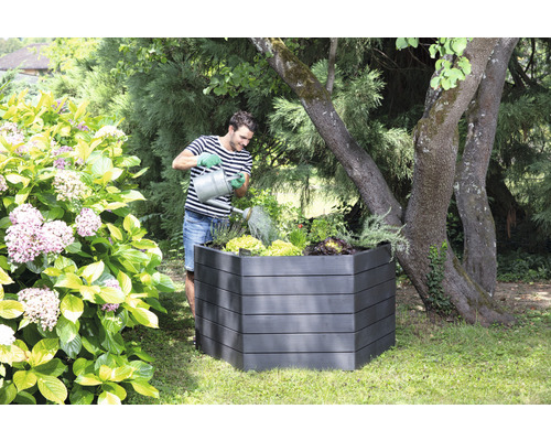 Mann giesst Pflanzen in einem Hochbeet im Garten.