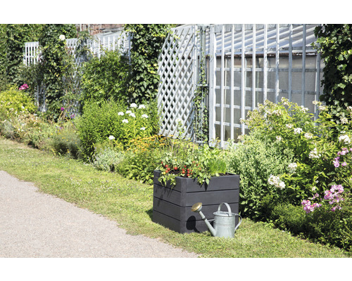 Gartenszene mit bepflanztem Hochbeet und Giesskanne vor einem Gartenzaun