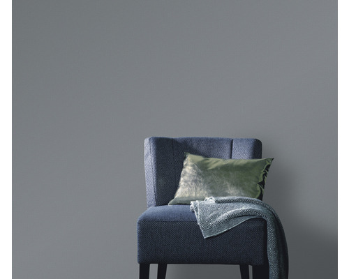 Einfarbige Tapete hinter einem Sessel mit Kissen und Decke