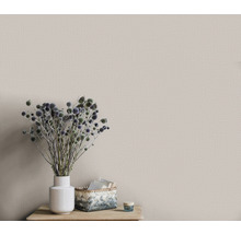 Gros plan d''un mur avec un papier peint textile beige, qui repose sur une table avec une composition florale dans un vase blanc et un panier.