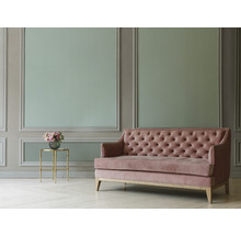 Gepolstertes Sofa mit Knopfheftung neben einem Beistelltisch mit Blumenstrauß vor einer verzierten Wand