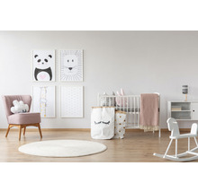 Helles Kinderzimmer mit Babybett, Sessel, Spielzeug, Teppich und Tierbildern an der Wand