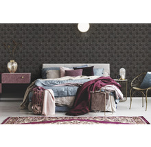 Schlafzimmer mit Bett, Nachttisch, Sessel und geometrischer Tapete