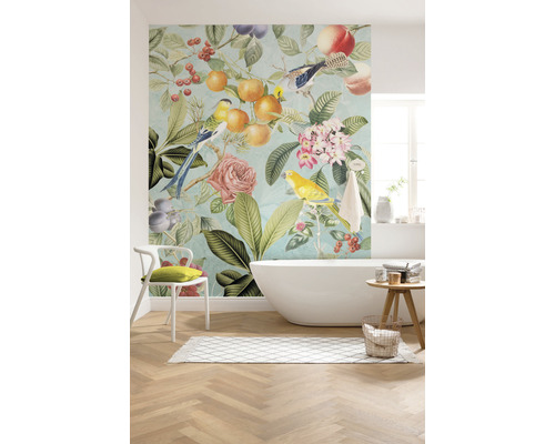 Salle de bains avec baignoire et papier peint mural avec motifs d''oiseaux, de fleurs et de fruits pour une ambiance lumineuse et conviviale.