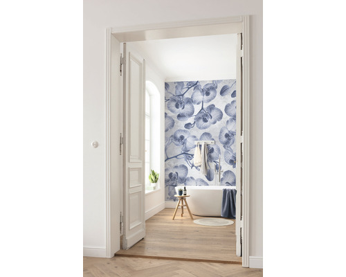 Salle de bains lumineuse avec baignoire, plancher en bois et papier peint photo à motif d''orchidées, photographiée à travers une porte ouverte.