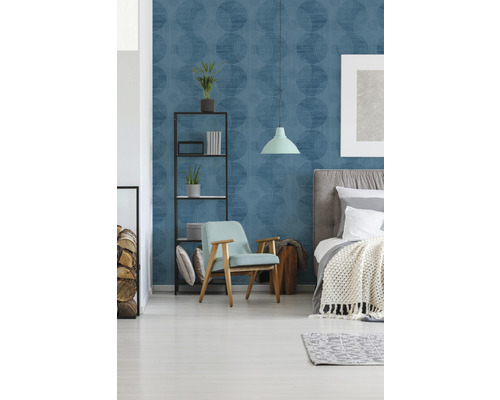 Schlafzimmer mit blau gemusterter Tapete, Bett, Sessel und Regal