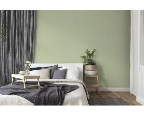 Schlafzimmer mit Bett, Nachttisch und dezent grün gestrichener Wand