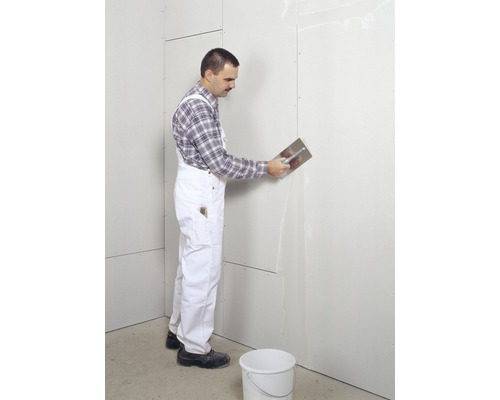 Artisan enduisant un mur en plaques de plâtre avec une spatule