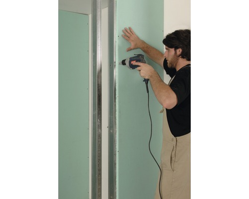 Un homme monte une cloison sèche avec une visseuse sans fil.