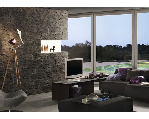 Wohnzimmer mit Steinwand, Fernseher, Lampe und Fensterfront mit Blick ins Grüne