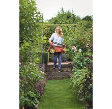 Frau trägt zusammengeklappten Rasenmäher im Garten.