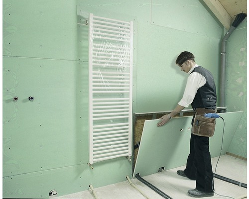 Ein Handwerker montiert eine Gipskartonplatte in einem Badezimmer mit Heizkörper.