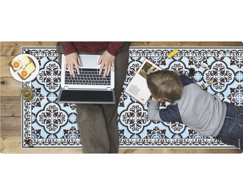 Bodenmatte mit Fliesenmuster, darauf eine Person mit Laptop und ein Kind mit einem Buch