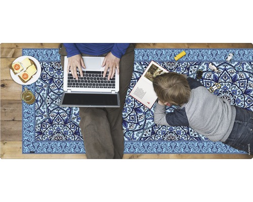 Szene mit einer Person, die einen Laptop benutzt, und einem Kind, das auf einem Spielteppich mit blauem Muster liegt