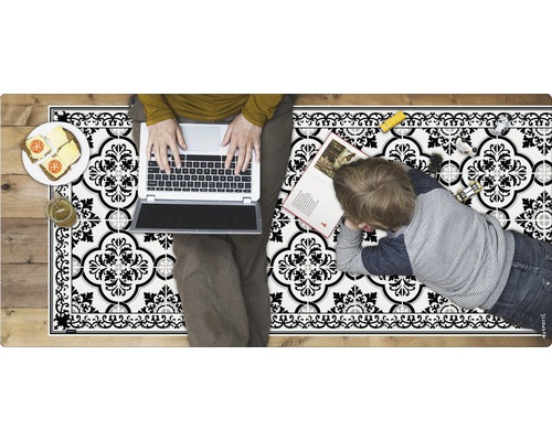 Bodenmatte mit Fliesenmuster, darauf eine Person mit Laptop und ein Kind mit Buch