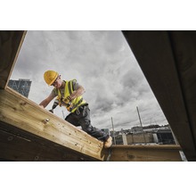 Artisan avec une perceuse travaillant sur une construction en bois à l''extérieur.