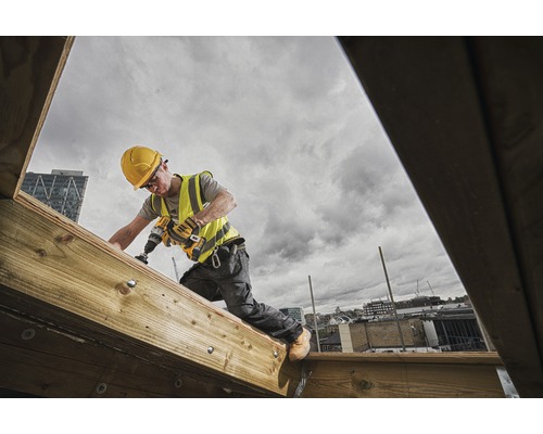 Artisan avec une perceuse travaillant sur une construction en bois à l''extérieur.