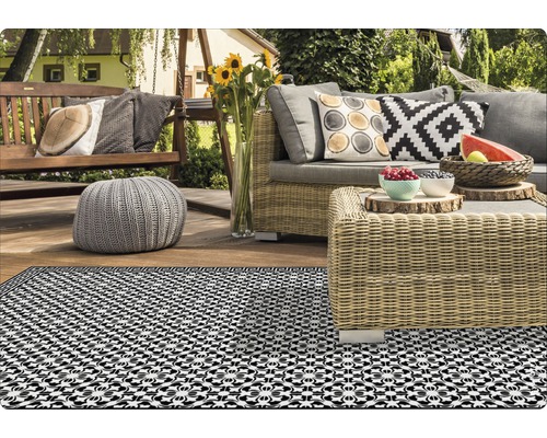 Terrasse mit Rattanmöbeln, Hängesessel und gemustertem Teppich für den Außenbereich.