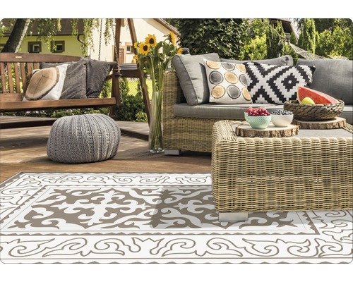 Gartenlounge-Bereich mit Rattansofa, Sitzbank, Hocker und gemustertem Teppich auf einer Holzterrasse