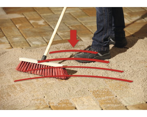 Une personne balaye le sable de jointoiement dans les joints de pavage avec un balai de voirie.