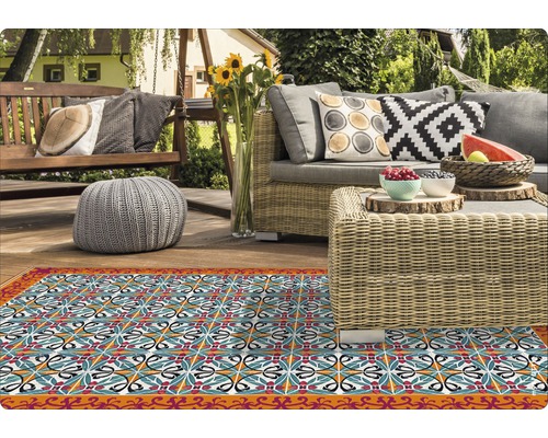 Terrassenszene mit gemustertem Teppich, Rattansofa und Holzbänken