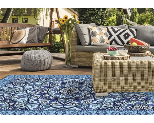 Szene mit Outdoor-Teppich, Gartenmöbeln und Dekorationen auf einer Terrasse