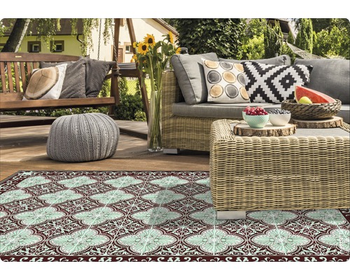 Szene mit Outdoor Teppich, Gartenmöbeln und Dekorationen auf einer Terrasse.