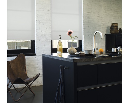 Cuisine lumineuse avec des stores enrouleurs blancs devant les fenêtres, un îlot de cuisine et un fauteuil en cuir.