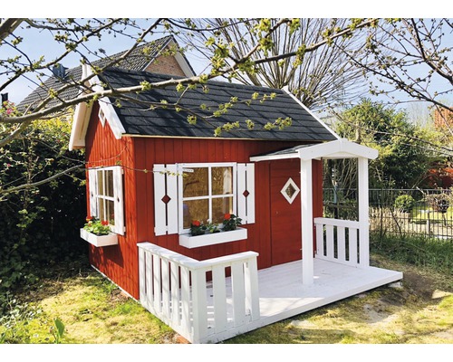 Rotes Spielhaus aus Holz mit weißem Geländer und Fensterläden im Garten.