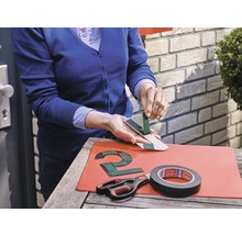 Person befestigt eine Hausnummer mit Klebeband