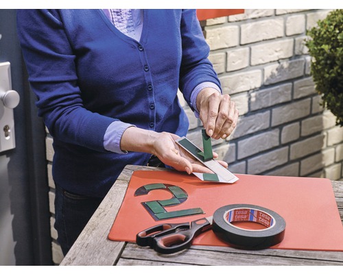Person befestigt eine Hausnummer mit Klebeband