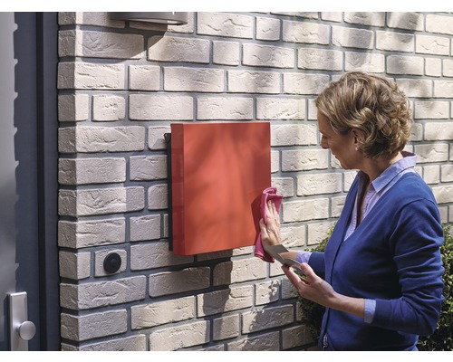 Frau reinigt einen roten Briefkasten an einer Backsteinmauer