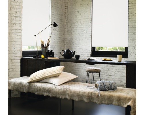 Pièce lumineuse avec des stores devant les fenêtres, une longue table servant de plan de travail et un coin salon confortable