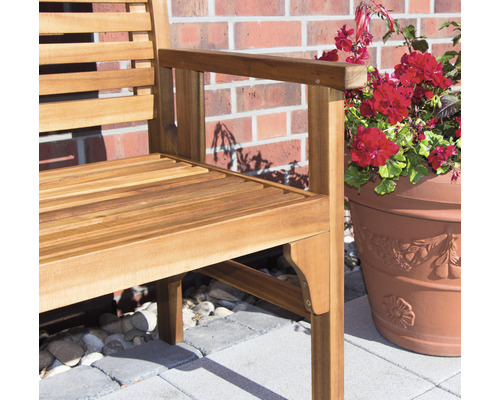 Detailansicht einer Gartenbank aus Holz mit Armlehne und einem Blumentopf mit roten Blumen