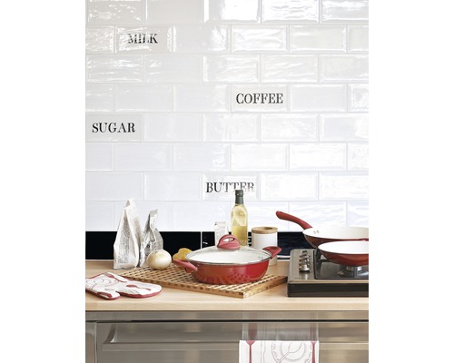 Küchenszene mit Kochtopf, Pfanne und Küchenutensilien vor weißer Fliesenwand