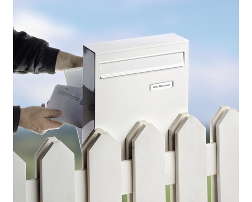Personne mettant du courrier dans une boîte aux lettres blanche à côté d''une clôture blanche