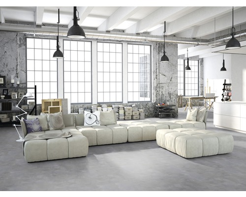 Salon lumineux de style loft avec canapé modulable, mur en béton et grandes fenêtres.