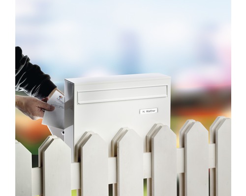 Person legt Brief in einen Briefkasten aus Metall an einem Gartenzaun