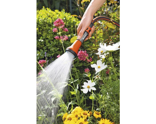 Une main tient une douche de jardin qui arrose les fleurs.