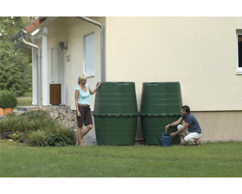 Deux récupérateurs d''eau de pluie verts dans le jardin devant une maison, un homme remplit un arrosoir
