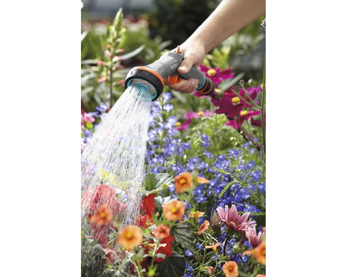 Une personne arrose des fleurs avec un pulvérisateur de jardin Gardena.
