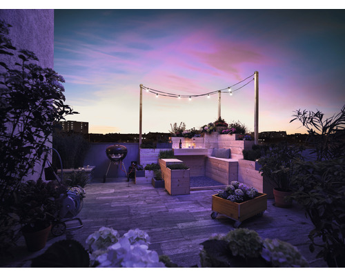 Terrasse sur le toit avec barbecue, meubles en bois, plantes et guirlande lumineuse au crépuscule