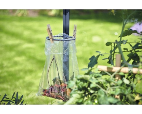 Poubelle avec des feuilles, fixée à un poteau, dans le jardin