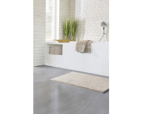 Salle de bain lumineuse avec tapis de bain, serviettes et décoration sur une baignoire maçonnée.