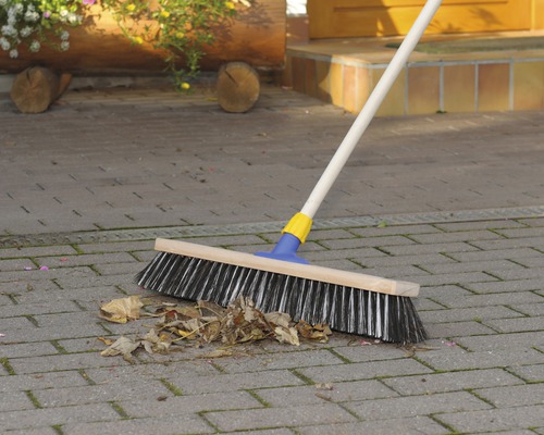 Balai de rue avec manche en bois et poils pour nettoyer les feuilles sur une surface pavée.