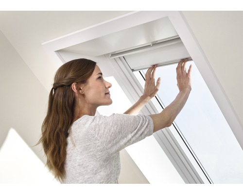 Une femme actionne une fenêtre de toit dans une pièce lumineuse.