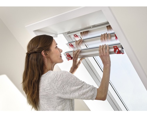 Femme actionnant une fenêtre de toit avec un store occultant.