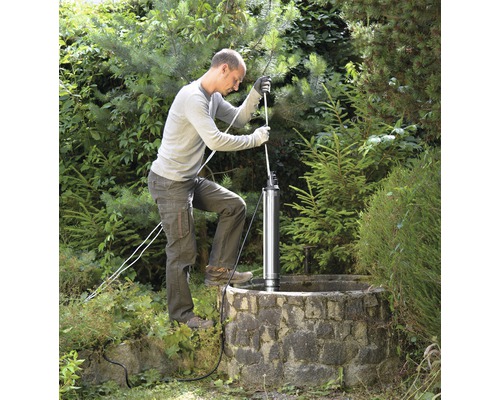 Un homme installe une pompe de puits profond dans un puits de jardin.